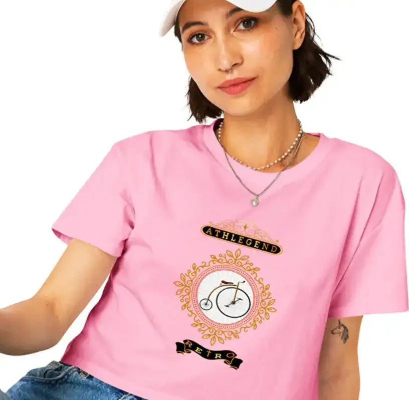 Pink short-sleeved t-shirt with a vintage bicycle graphic framed in gold and black ornamental details, featuring the text ’athlegend’ above and ’retr0’’ below.